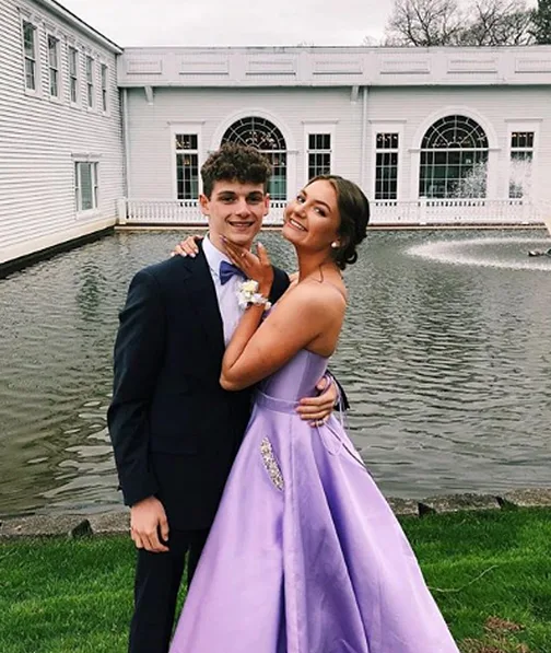 Young man and woman dressed for prom pose next to pond
