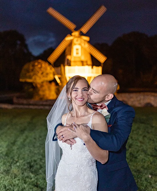 Bride and groom stand in front of the windmill at night