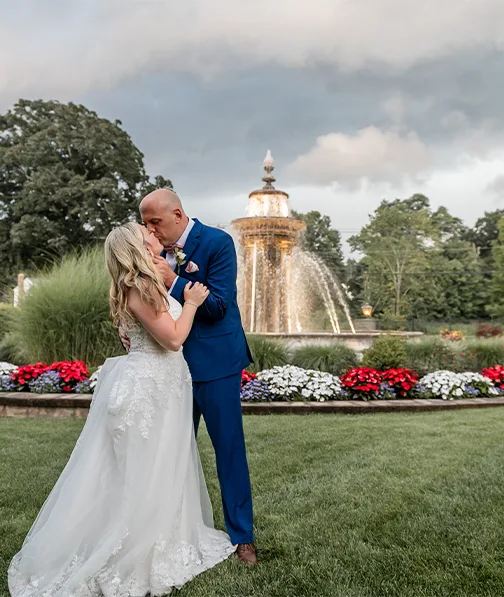 Bride and groom kissing with flower and fountain in the background